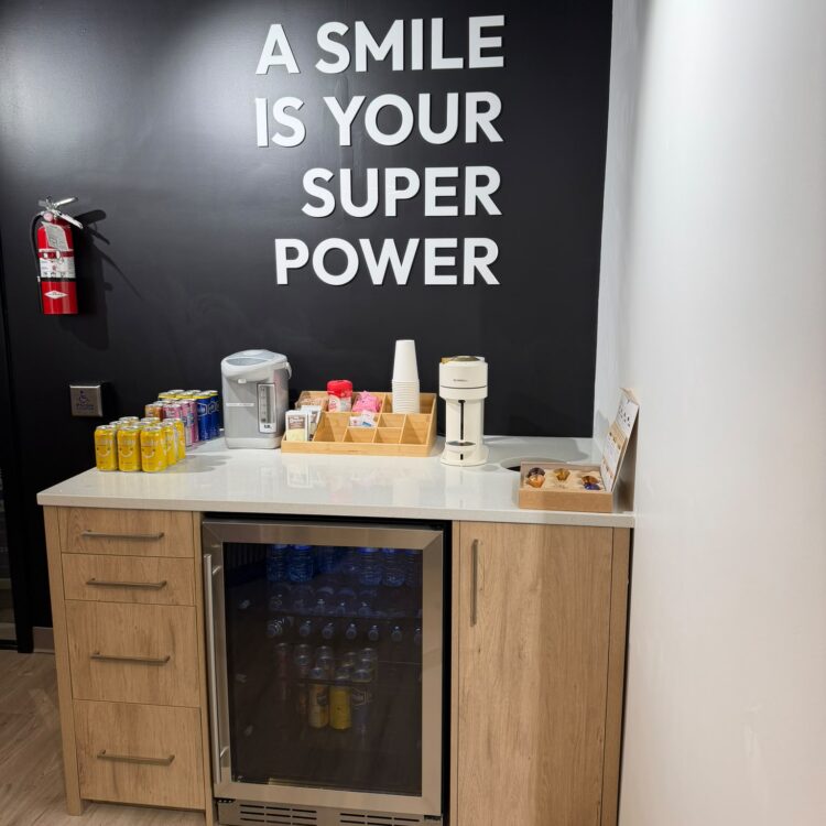 Patient coffee and refreshment bar under an "A smile is your super power" wall at Smili Dental