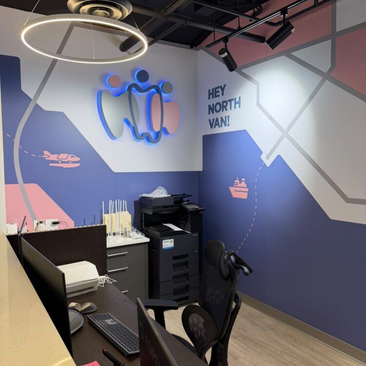 Illuminated Smili Dental logo and "Hey North Van!" mural behind the front desk