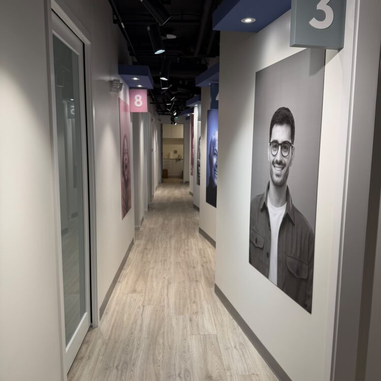 Hallway to numbered dental treatment rooms with smiling patient portraits at Smili Dental